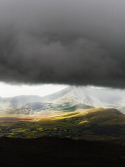 Sunlight breaks through storm clouds over the mountains of County Kerry, Ireland.