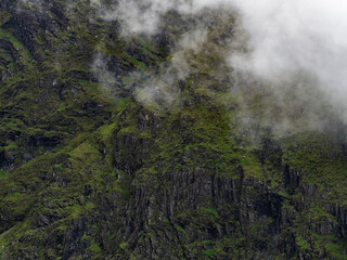Landscape shows mountain rock face with green moss and low lying mist.
