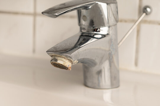 Close-up of a worn bathroom faucet with visible limescale and corrosion on the aerator, illustrating problems caused by hard water, mineral buildup, and lack of plumbing maintenance.