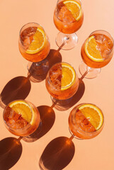 Top-down view of Aperol Spritz cocktails with orange slices on a monochrome background. Bright, direct sunlight creates long, dramatic shadows. Summer party concept.