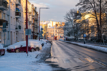 Winter urban street in morning light reveals a calm landscape. Snow, parked cars and tenements shape everyday city silence during early winter