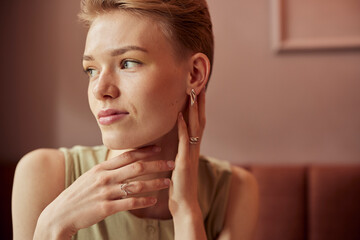Portrait of a thoughtful short-haired woman in a cafe wearing delicate jewelry and soft lighting