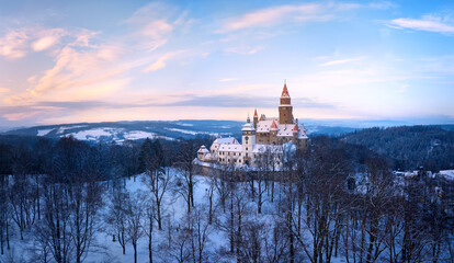 Bouzov Castle in winter landscape at sunrise, historic medieval fortress surrounded by snowy forest, Czech Republic