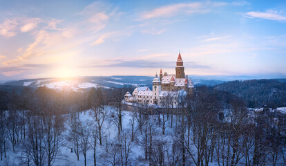 Bouzov Castle in winter landscape at sunrise, historic medieval fortress surrounded by snowy forest, Czech Republic