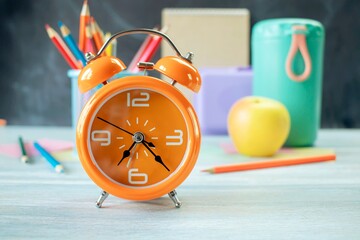 Alarm clock, water, lunchbox, apple and school supplies on table, back to school