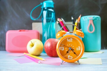 Alarm clock, water, lunchbox, apple and school supplies on table, back to school