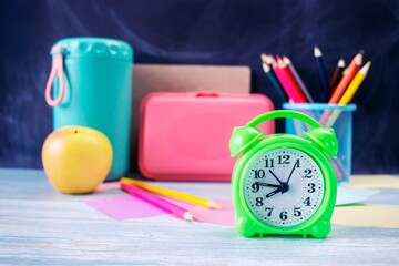 Alarm clock, water, lunchbox, apple and school supplies on table, back to school