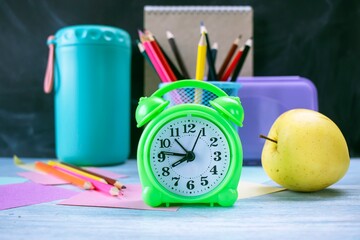 Alarm clock, water, lunchbox, apple and school supplies on table, back to school
