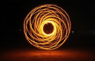 Fire poi creates spiral motion pattern in show. Long exposure captures light painting effect in darkness. Creative art performance with flame spinning entertains audience. Festival event at night