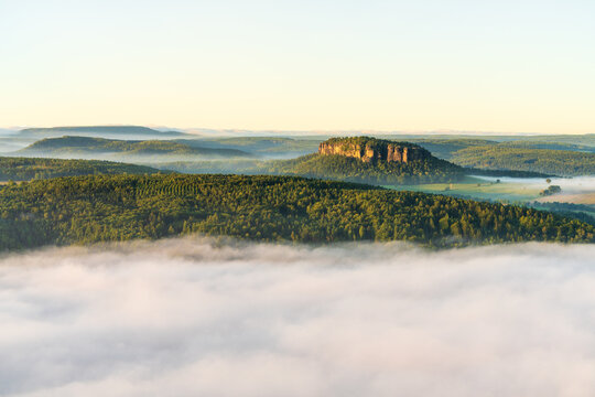 Beautiful summer landscape of Saxon Switzerland National Park in Germany. Isolated Pfaffenstein mountain rising above dense fog. Scenic nature travel and outdoor concept.