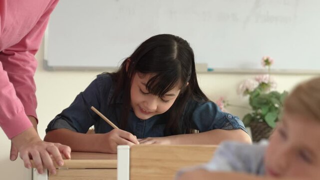 Asian girl writing or taking a note while teacher checking classwork. Caucasian teacher help happy student doing test or classwork while diverse student study in science lesson. Education. Pedagogy.