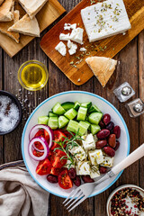 Greek salad - tomatoes with feta cheese, cucumber, red onion and kalamata olives on wooden table. Top view