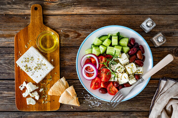 Greek salad - tomatoes with feta cheese, cucumber, red onion and kalamata olives on wooden table. Top view