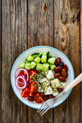 Greek salad - tomatoes with feta cheese, cucumber, red onion and kalamata olives on wooden table. Top view