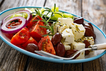 Greek salad - tomatoes with feta cheese, cucumber, red onion and kalamata olives on wooden table