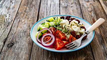 Greek salad - tomatoes with feta cheese, cucumber, red onion and kalamata olives on wooden table