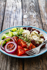 Greek salad - tomatoes with feta cheese, cucumber, red onion and kalamata olives on wooden table