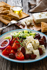 Greek salad - tomatoes with feta cheese, cucumber, red onion and kalamata olives on wooden table