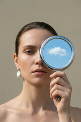 A conceptual art portrait of a woman covering her eye with a mirror reflecting a blue sky. A concept of imagination, dreams, and a clear mind.