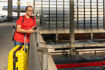 Fototapeta premium Man with yellow suitcase overlooking trains at railway station
