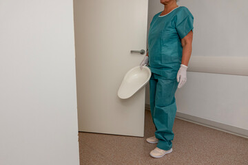 A medical worker stands in a room by a door with a bedpan