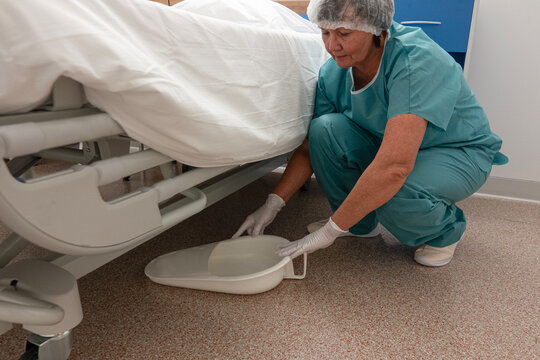 Nurse picks up a portable urinal from the floor in a hospital
