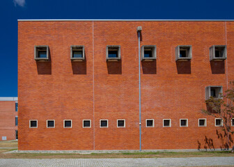 Fachada minimalista de tijolo vermelho com simetria geom&eacute;trica nas janelas.