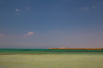 Quebra-mar tranquilo com farol, c&eacute;u azul e mar calmo.