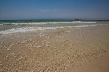 Quebra-mar tranquilo com farol, c&eacute;u azul e mar calmo.