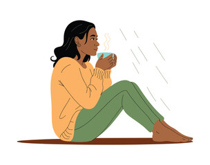 Woman in orange sweater and green pants holding a blue coffee cup with steam.