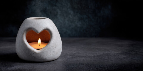 Cozy ceramic oil burner heart shape tealight candle soft flame romantic mood spa decor minimal style gray stone warm glow zen calm. Gentle smoke drifts in dark room relaxing ambiance