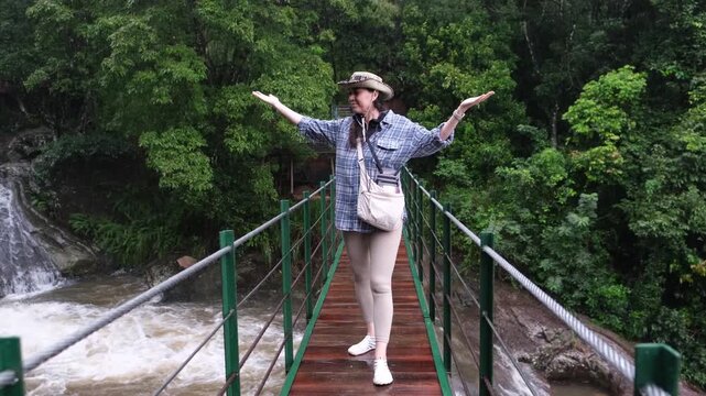 Young woman standing on a suspension bridge above Bambarakiri Ella in Sri Lanka. Female traveler enjoying nature, adventure travel and tropical landscape, freedom and exploration concept.