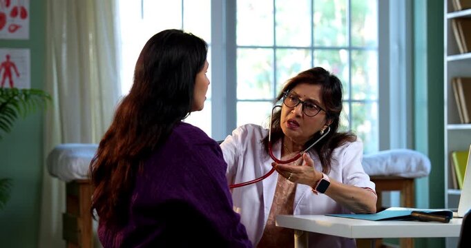 Experienced Indian lady doctor woman checking young female patient in clinic using stethoscope, torch and pulse examination during routine health checkup in modern medical facility