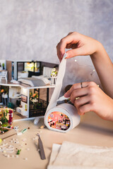 Girl's hand gluing fabric to tiny roombox on table vertical view