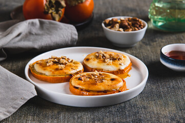 Delicious baked persimmon with cottage cheese, nuts and honey on a plate on the table