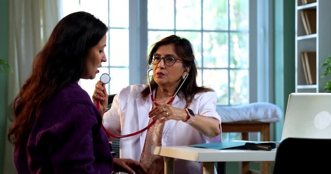 Experienced Indian lady doctor woman checking young female patient in clinic using stethoscope, torch and pulse examination during routine health checkup in modern medical facility