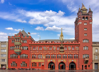 Historic red town hall in Basel with ornate facade, clock tower, painted murals, and bicycles in the city square under a blue sky. © Vladislav Gajic