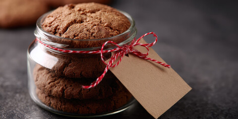 Homemade cookie mix glass jar kraft tag red twine rustic gift baked cookie dessert sweet treat cozy kitchen dark background. Homemade cookie mix glass jar with kraft tag and red twine