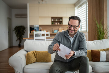 Happy man opening mail at home enjoying positive news