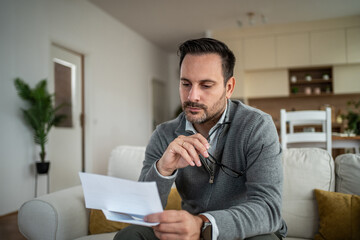 Man evaluating finances at home reading letter feeling stressed