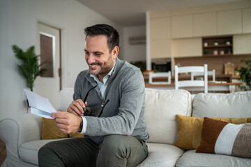 Fototapeta premium Happy man smiling reading good news letter at home