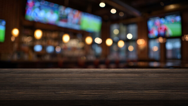 Wooden tabletop and blurred abstract background of a sports bar with screens and broadcasts