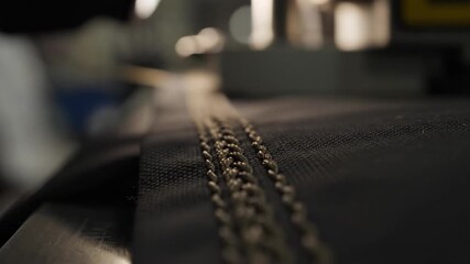 Close-up of a black fabric with two gold zippers being sewn on an industrial sewing machine in a factory