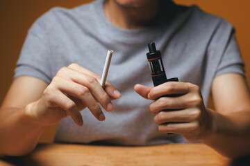 Man holding vape and tobacco cigarette on desktop - Quit Smoking concept
