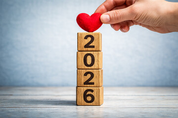 Hand placing red heart on wooden year blocks symbolizing care