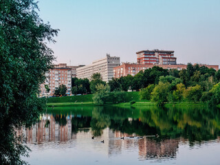 Obraz premium serene urban landscape featuring a calm pond surrounded by greenery and residential buildings
