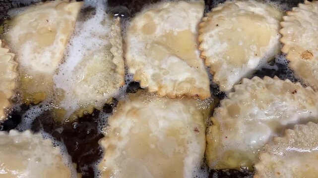 A close-up of a professional kitchen frying chebureki in a deep fryer. Chebureki have a golden, crispy crust and a juicy meat filling. Traditional Eastern street food