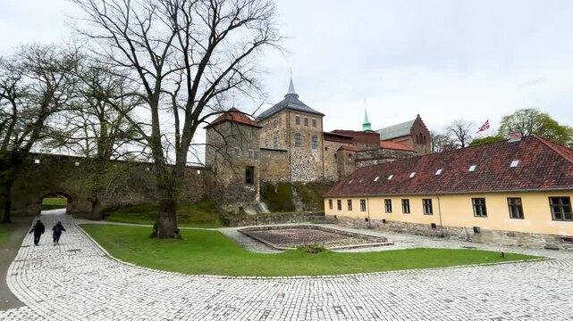 akershus fortress stone towers walls above yellow barracks building cobblestone walkways lawns trees visitors define scene oslo norway broad view historic citadel 