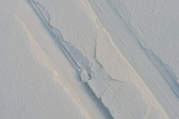 Beautiful winter background with snow-covered ground. Ski tracks in the snow. Rhythmic linear patterns and winter texture on snow. Artificial snow texture.