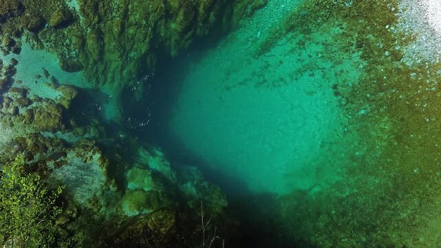 Aerial top view of turquoise spring water surrounded by lush green forest, Oko Skakavice in Montenegro, 4k